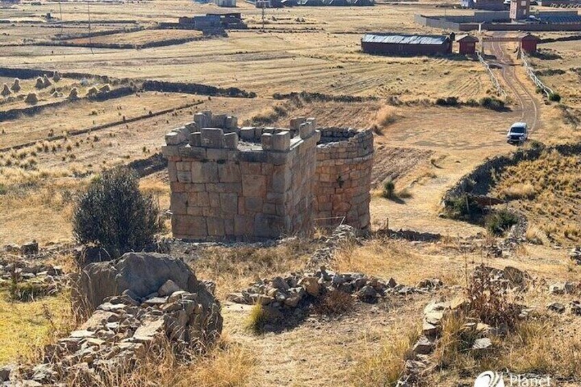 A stone castle ruin surrounded by dry grassland and distant buildings. 4