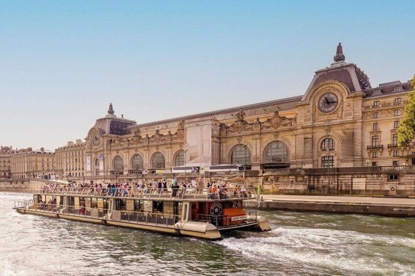 A river cruise boat with passengers, a large historic building with a clock tower, and a clear sky. 5