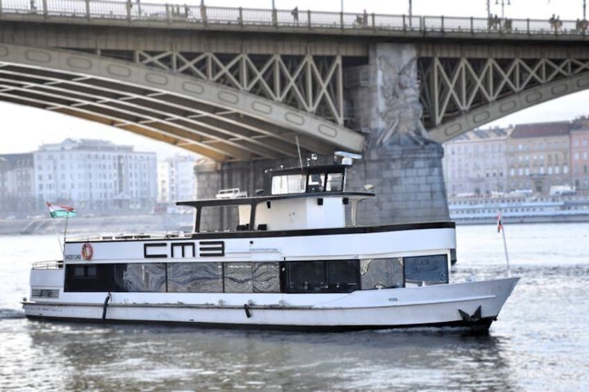A white boat with 'CMA' on its side, docked under a bridge with a statue on the pillar. 3