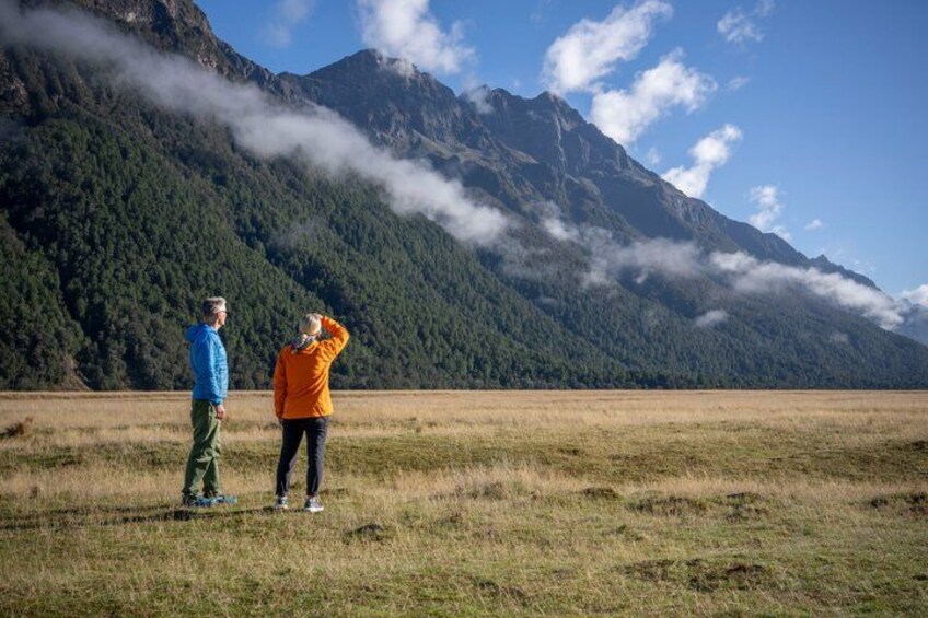 Zwei Personen stehen auf einem Feld, im Hintergrund erstreckt sich eine Bergkette. 5