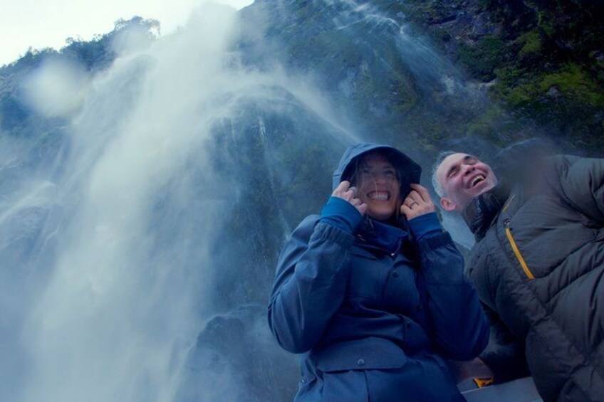 Ein Wasserfall mit Nebel, eine Person in einer blauen Jacke und eine weitere in einer grauen Jacke. 4