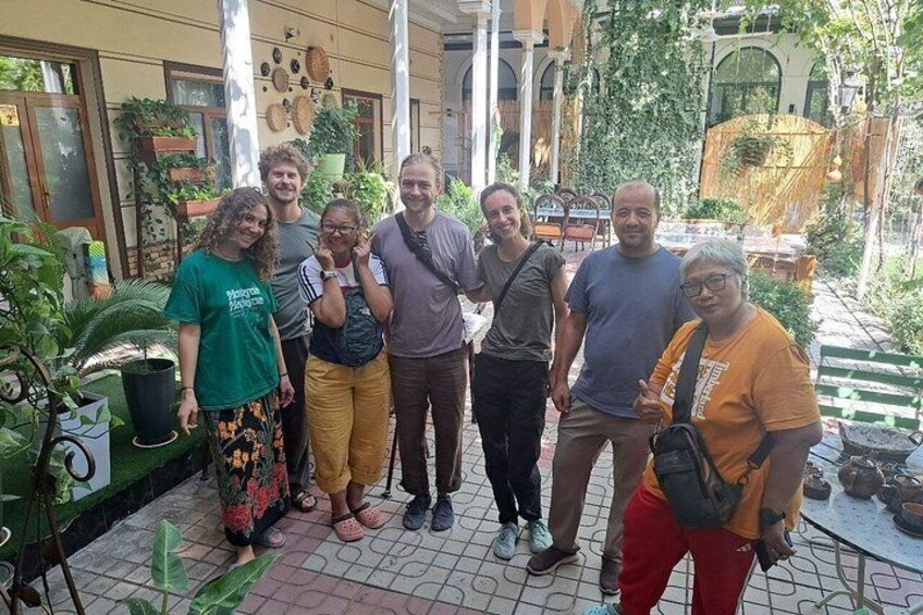 A group of people standing in a courtyard with potted plants and a table with items on it. 2