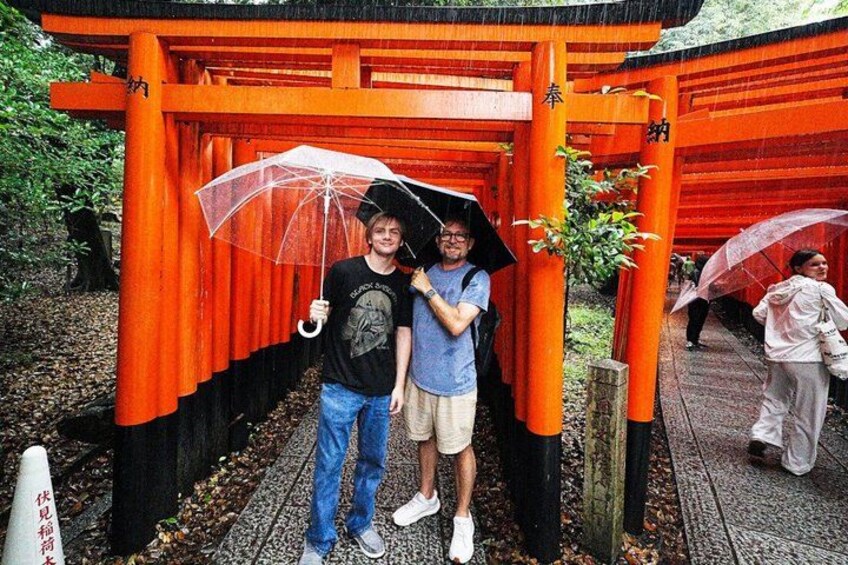 Two people standing under a red torii gate with umbrellas. 5