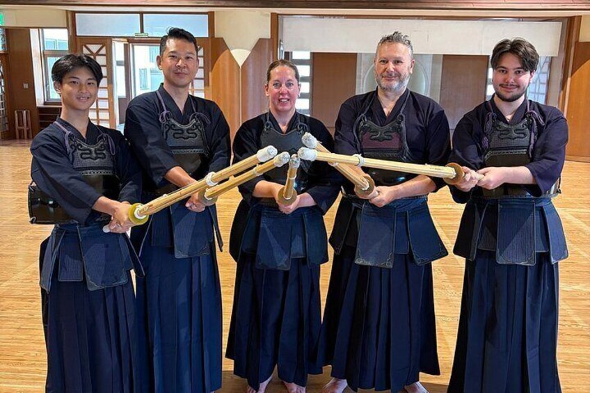 Five people in traditional martial arts attire holding wooden staffs. 5