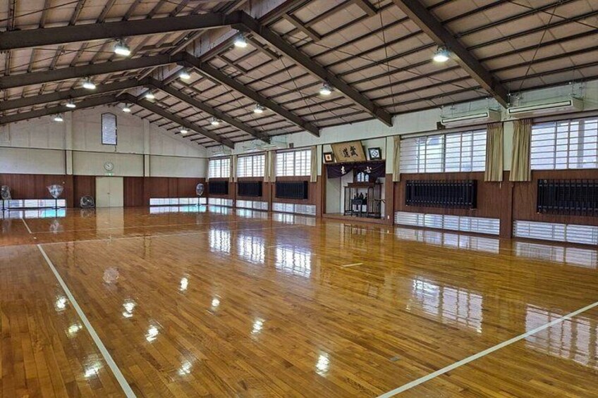 An indoor sports hall with a polished wooden floor, high ceilings, and large windows. 2