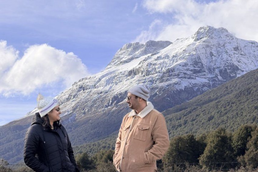 Two people standing in a mountainous area with snow-capped peaks in the background. 3