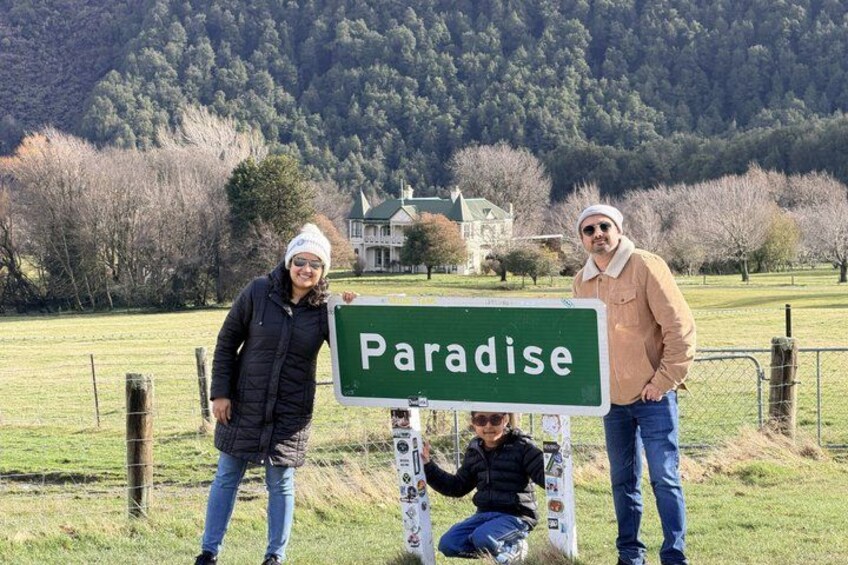 Three people standing in front of a green sign that reads 'Paradise.' 5