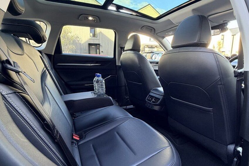 A car's interior with black leather seats, a sunroof, and a bottle of water on the passenger seat. 3