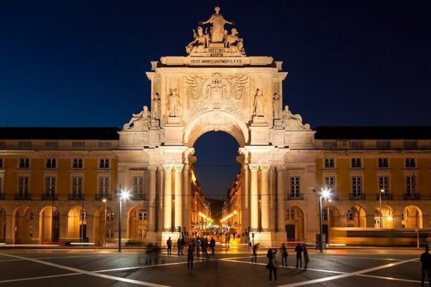 A grand illuminated archway with classical sculptures, surrounded by a bustling square with people and street lamps. 2