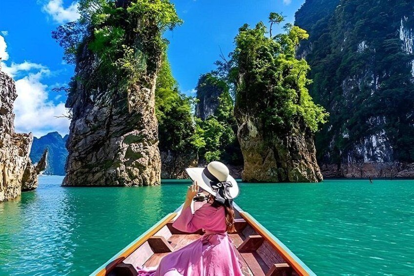 A boat with a person wearing a pink dress and a white hat, surrounded by turquoise water and rocky cliffs. 2