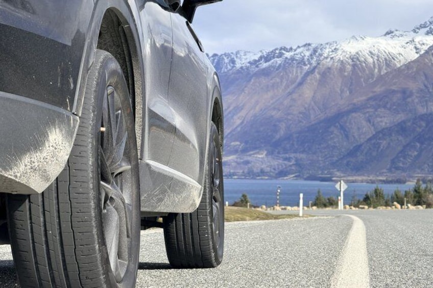 A car's rear wheel on a road with a mountainous landscape in the background. 2