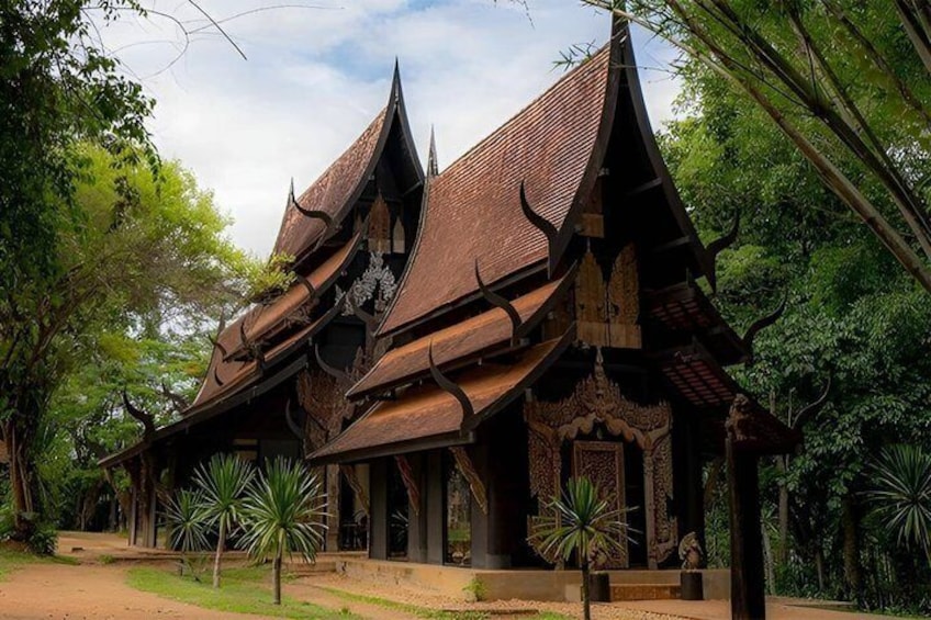 A traditional wooden structure with a steeply pitched roof, surrounded by lush greenery. 1
