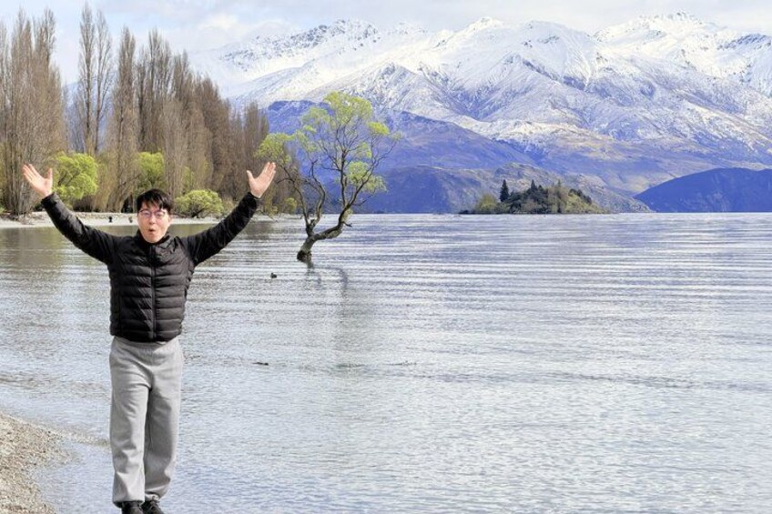 A person standing in a lake with arms raised, trees, and snow-capped mountains in the background. 3