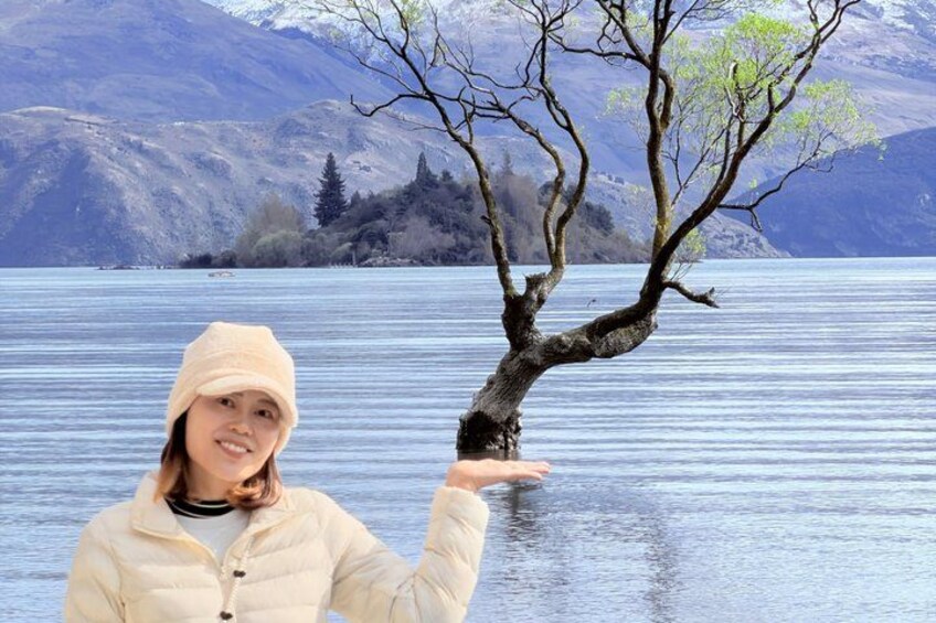 A person standing by a lake with a tree in the foreground and mountains in the background. 4