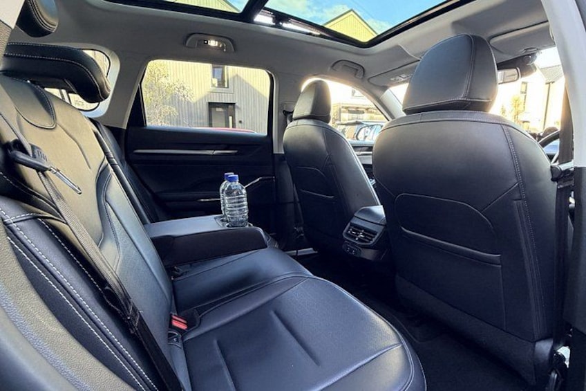 A car's interior with black leather seats, a sunroof, and a bottle of water on the passenger seat. 3