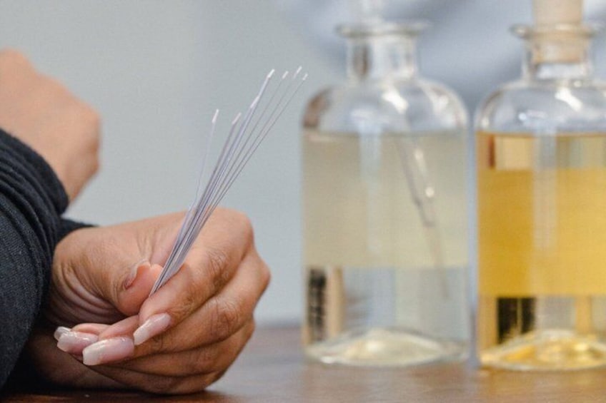 A hand holding incense sticks with two glass bottles in the background. 1
