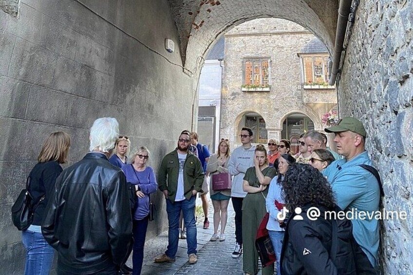 A group of people standing in a stone archway, with a building in the background. 1