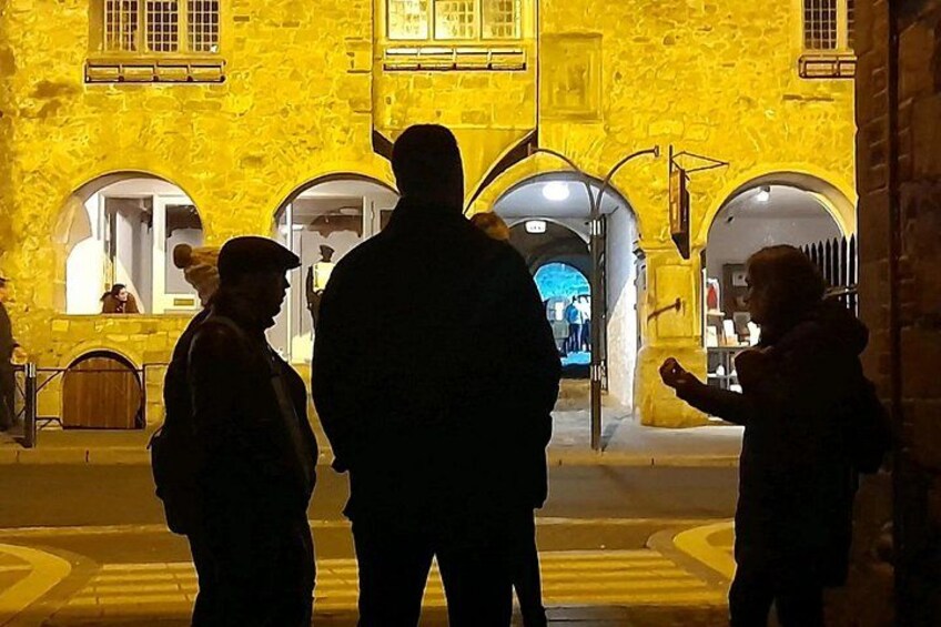 A group of people standing in front of a yellow building with arched doorways. 2