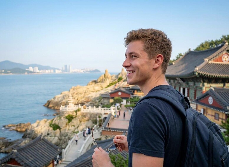 A person holding sunglasses overlooking a coastal area with traditional architecture and a rocky shoreline. 2