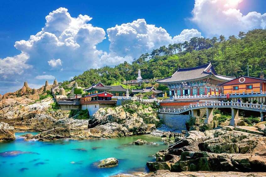 A traditional Chinese temple complex with a bridge over a turquoise river, surrounded by rocky terrain and lush greenery. 5