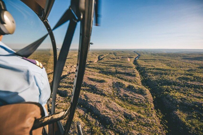 A helicopter's cockpit with a view of a river winding through a forested landscape. 2