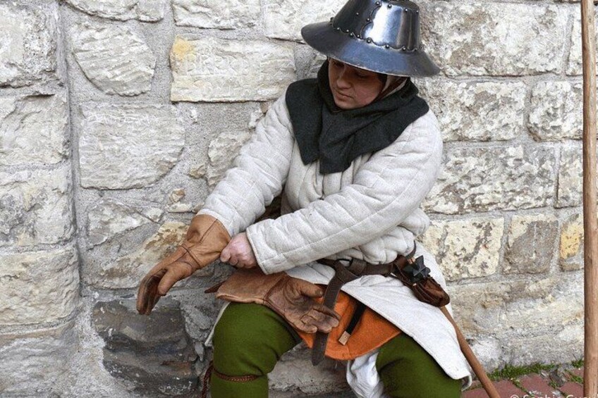 A person in medieval costume sitting against a stone wall. 5