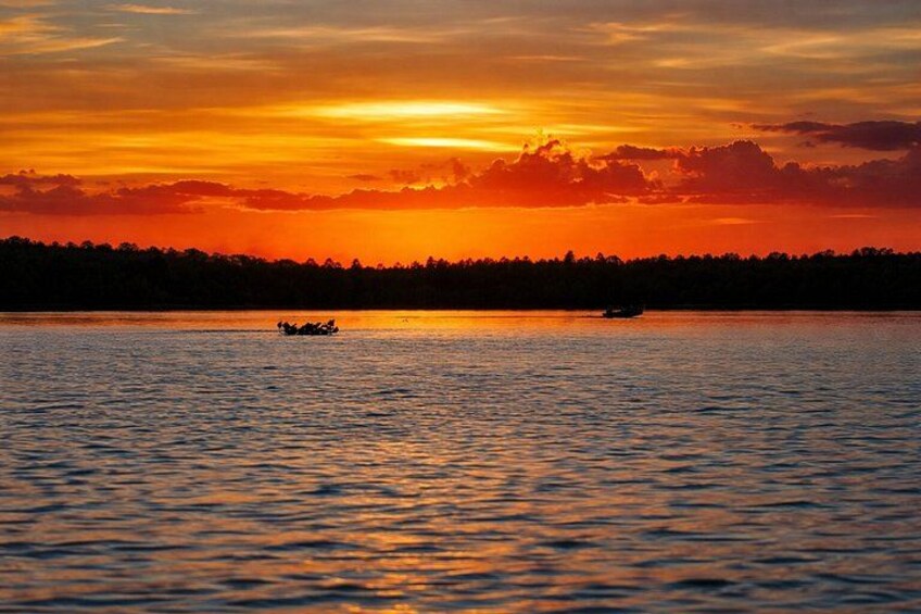 A sunset over a calm lake with a boat in the foreground and a forested shoreline. 4