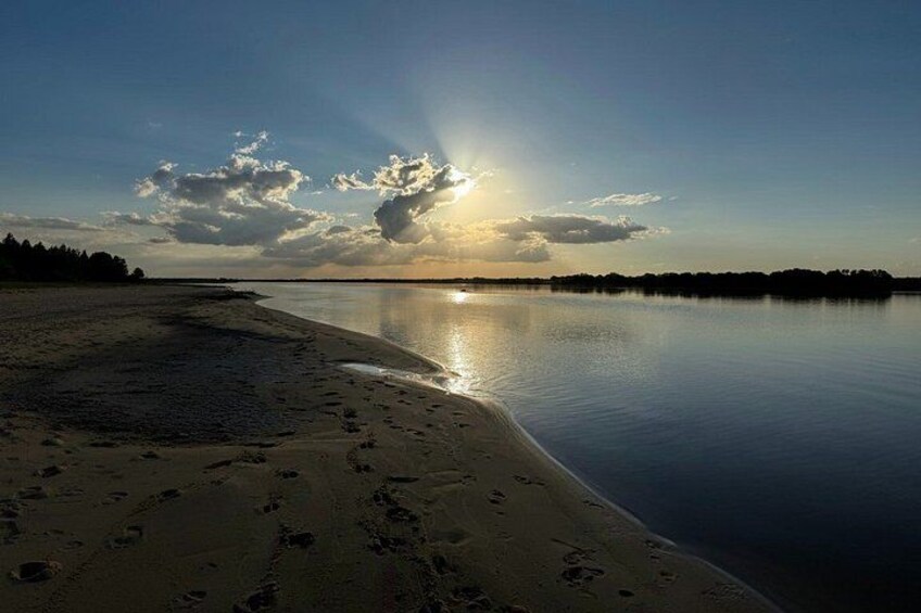 A calm lake at sunset with a sandy beach and a forest in the background. 5