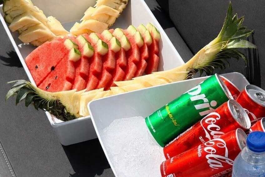 A tray with sliced watermelon and pineapple, a can of Dr. Pepper, and two cans of Coca-Cola. 3