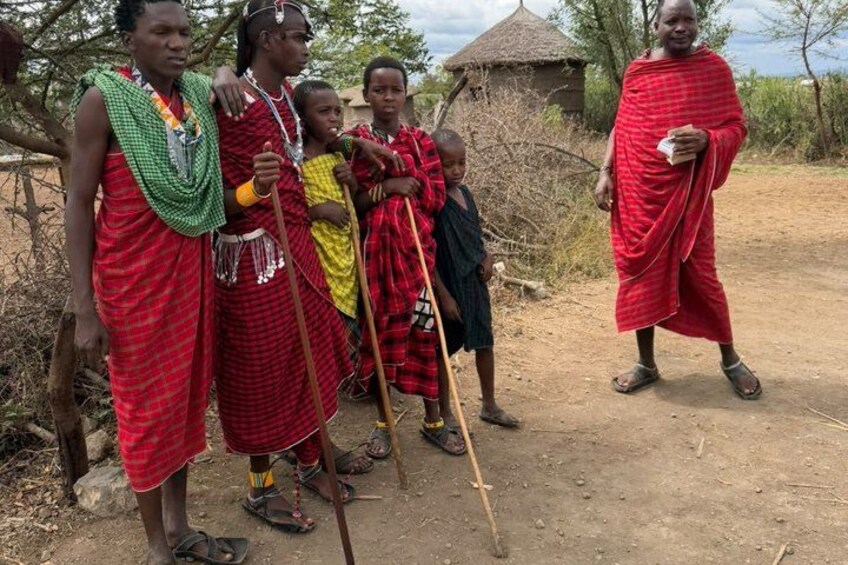 Persone Maasai in abiti tradizionali, una capanna con tetto di paglia e un sentiero sterrato. 3