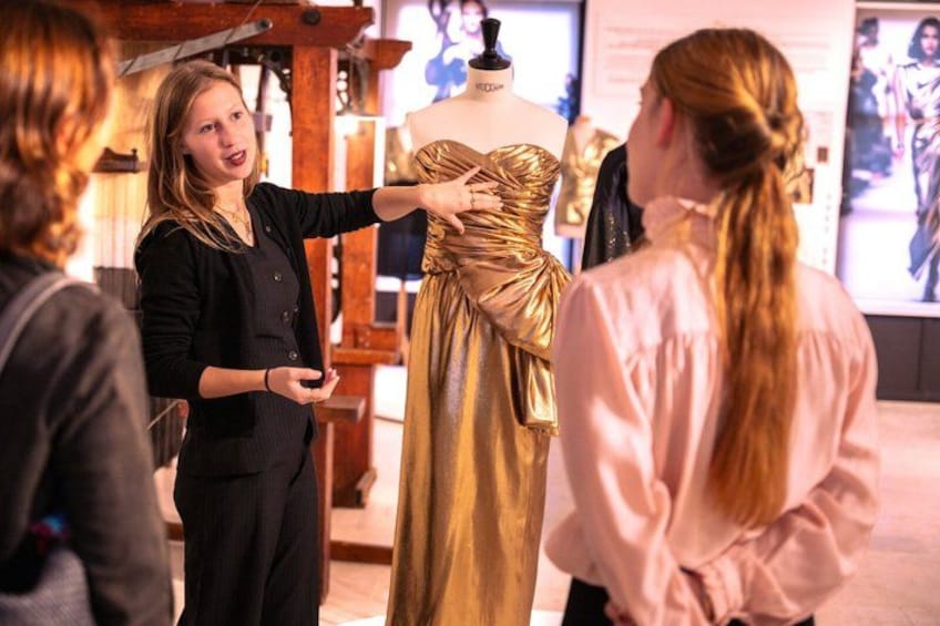 A person presenting a golden dress to a group of people. 1