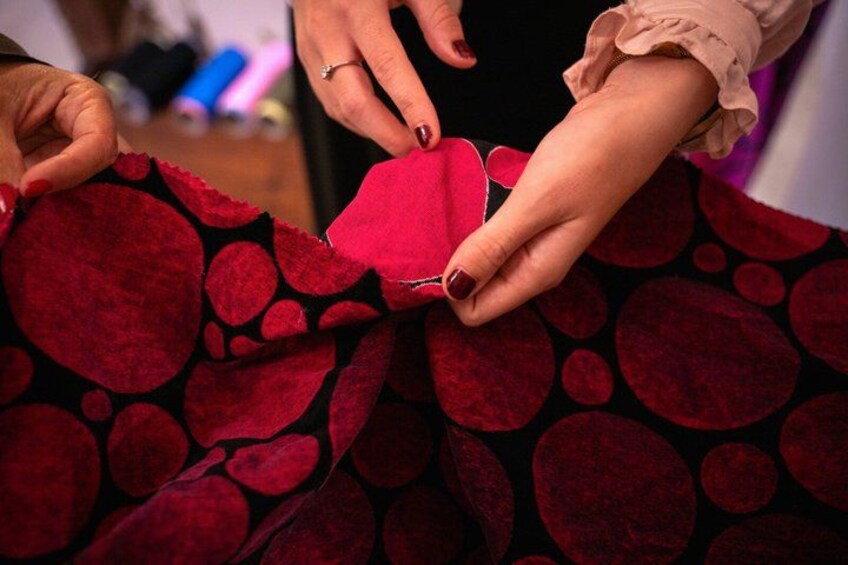 Hands sewing a red fabric onto a black background with red circular patterns. 5