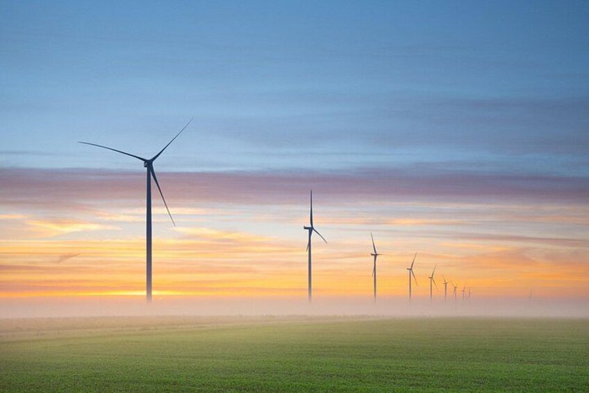 A wind farm with multiple wind turbines in a field during sunset. 3