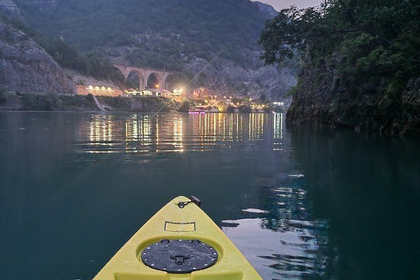 A yellow kayak on calm water with a bridge and lights in the background. 3