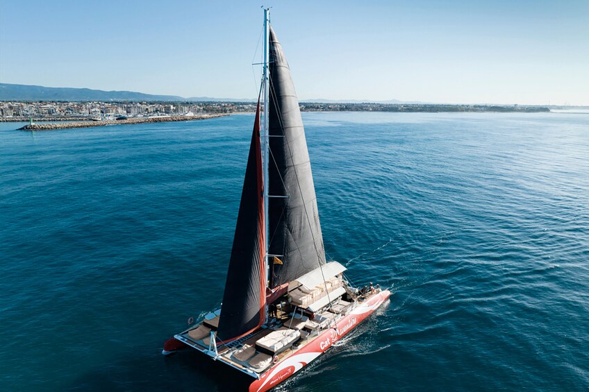 A sailboat with a black sail on a calm sea, with a cityscape in the background. 3