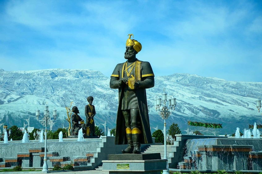 A statue of a historical figure in a park with snow-capped mountains in the background. 1