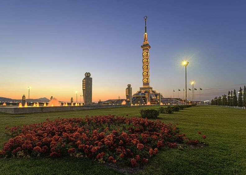 A tall tower with a spire, surrounded by a well-maintained lawn with red flowers, and a building with a unique design in the background. 3