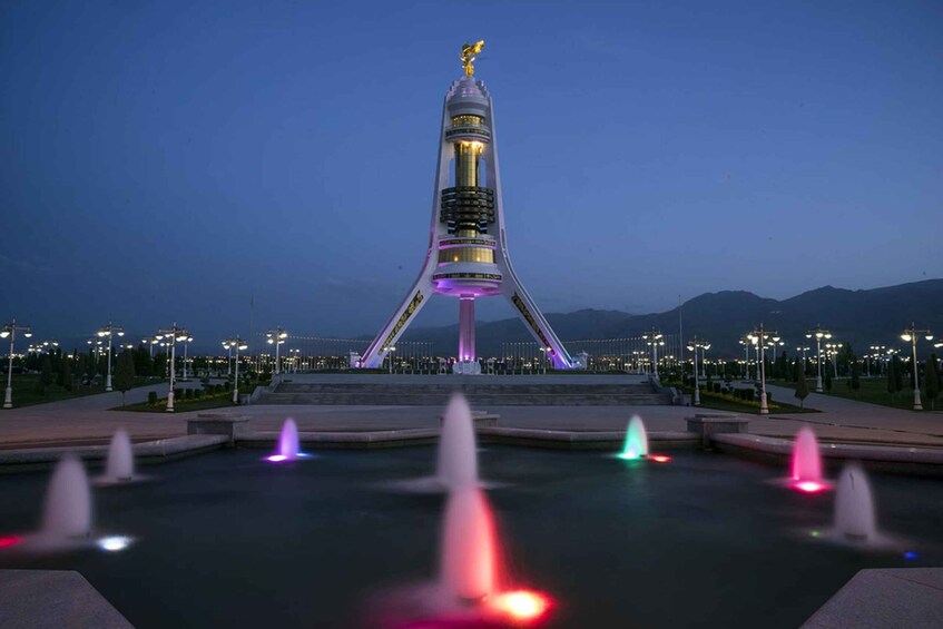 A tall tower with a golden statue on top, surrounded by a water feature with fountains. 5