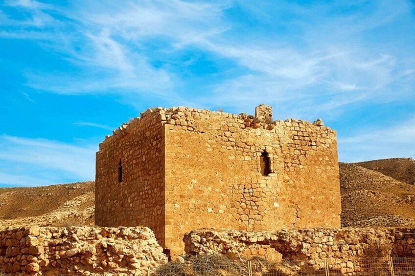 A stone building with a square base and a flat roof, surrounded by dry, rocky terrain. 3