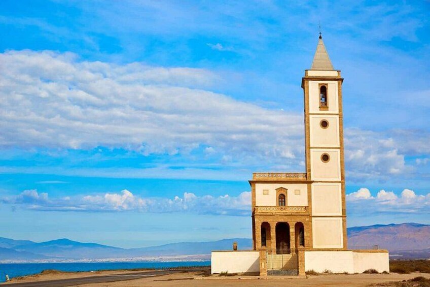 A coastal tower with a clock, surrounded by a clear sky and distant mountains. 5