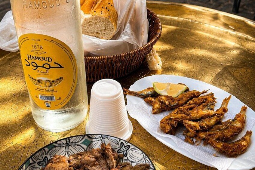 A bottle of Hamoud, a plate of fried fish, and a basket of bread on a table. 5