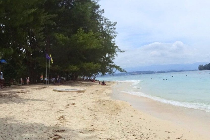 A beach with a row of trees, a flagpole, and a calm sea. 4