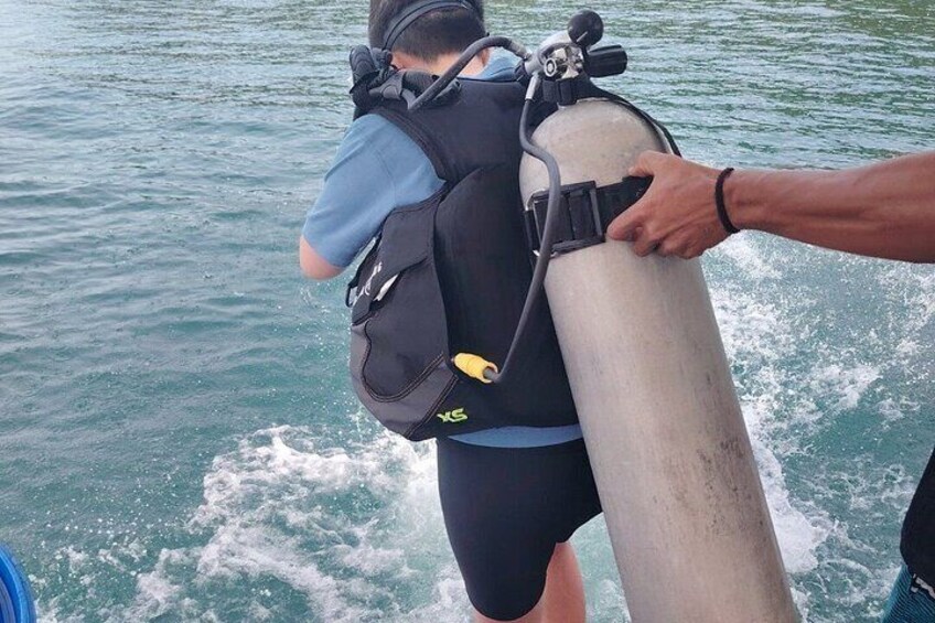 A person wearing a scuba diving mask and a black backpack, holding a large cylindrical object. 5