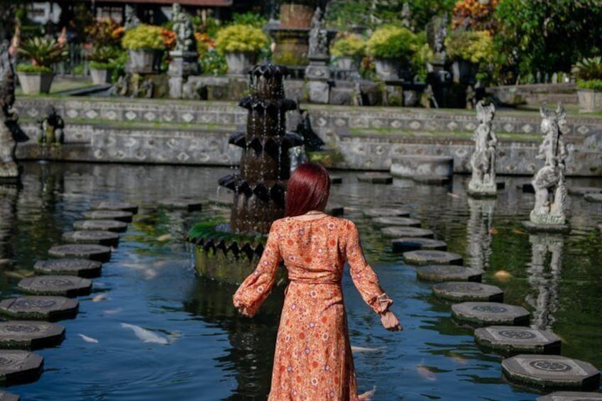 A woman in a patterned dress standing by a pond with stepping stones and a fountain. 5
