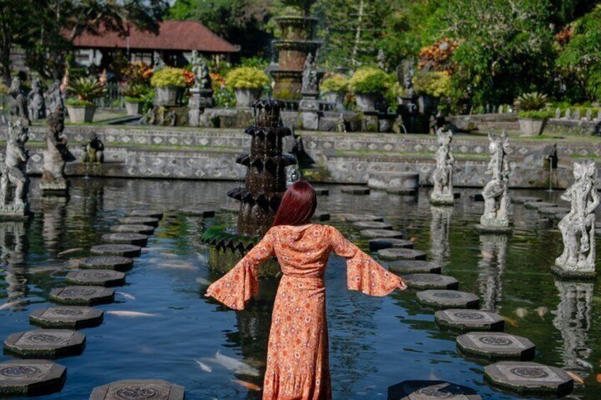 A woman in a patterned dress standing in a water garden with stepping stones and statues. 4