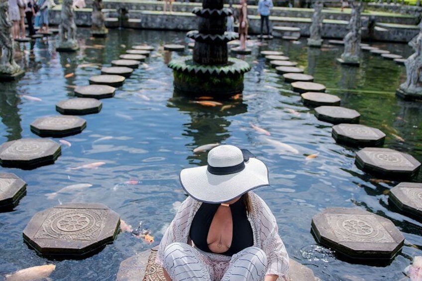 A person sitting by a pond with stepping stones, surrounded by statues and a fountain. 2