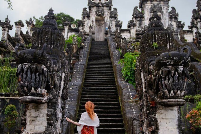 A woman standing at the base of a temple staircase with ornate lion statues on either side. 1