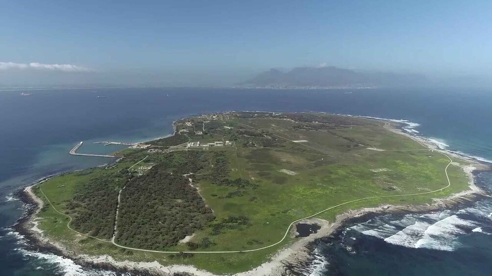 An aerial view of a coastal area with a mix of forested and open land, a curved road, and a clear view of the ocean. 4