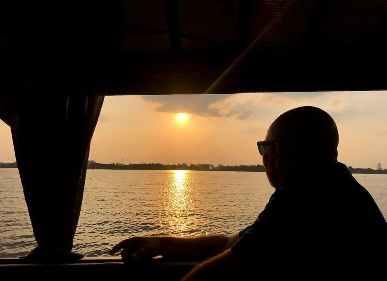 A person seated by a window, overlooking a sunset over a body of water with a distant shoreline. 1