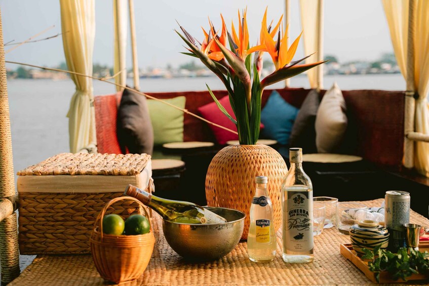 A wicker basket with lemons, a metal bowl, a bottle of gin, a can of soda, and a decorative bird of paradise flower on a boat deck. 3